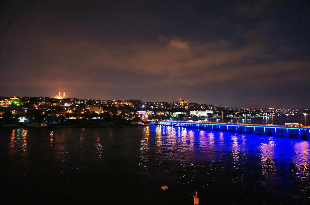 A lit up bridge leading to a lit up mosque under a rainy sky